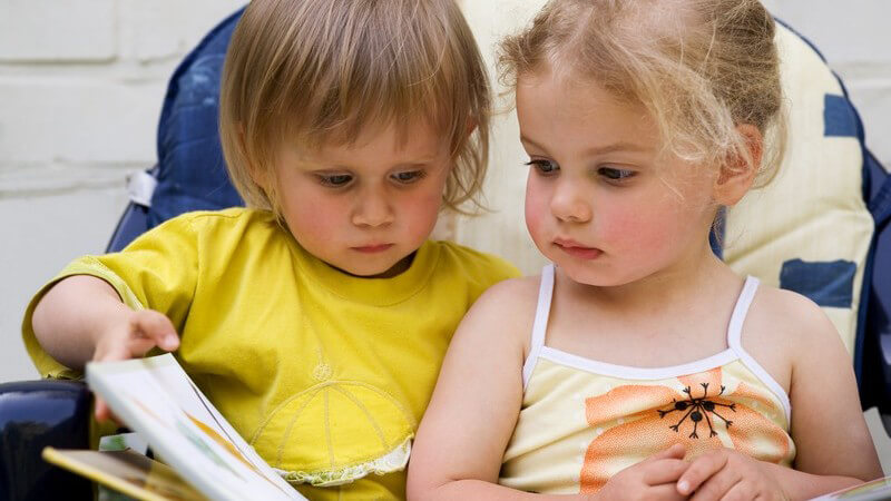 Junge im gelben Shirt und kleines Mädchen im Top lesen in einem großen Buch