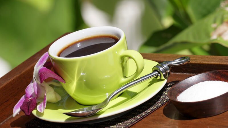 Nahaufnahme grüne Tasse Kaffee mit pinker Blüte