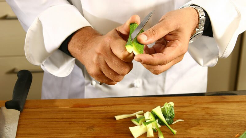 Koch schneidet Zucchinistifte auf einem Holzbrett