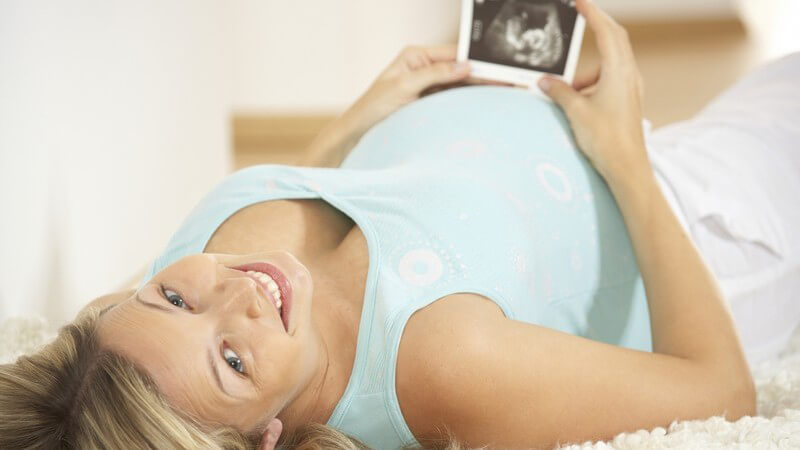 Schwangere Frau liegt auf Rücken, hält Ultraschallbild in Händen