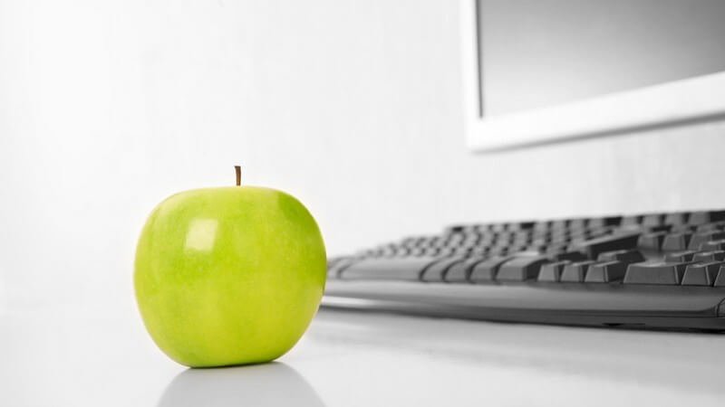Grüner Apfel auf Tisch vor Computertastatur
