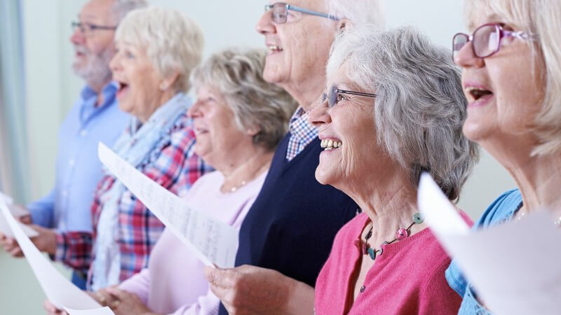 Sechs Senioren halten Notenblätter und singen fröhlich im Chor
