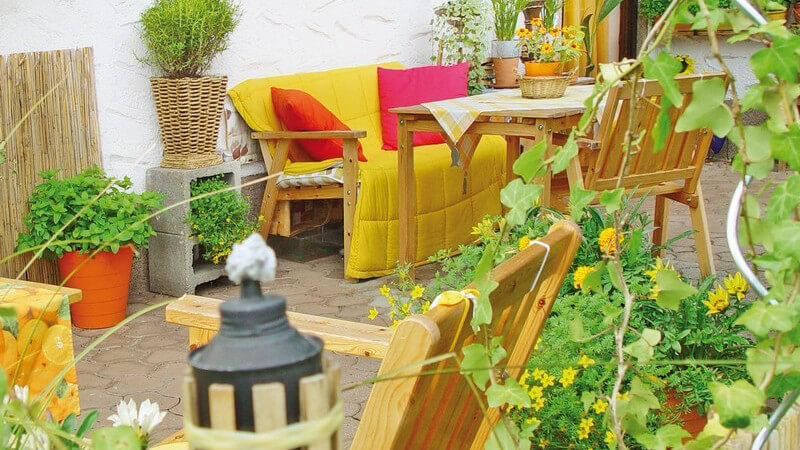 Terrasse mit Holzmöbeln und Fackel umgeben von vielen grünen Pflanzen
