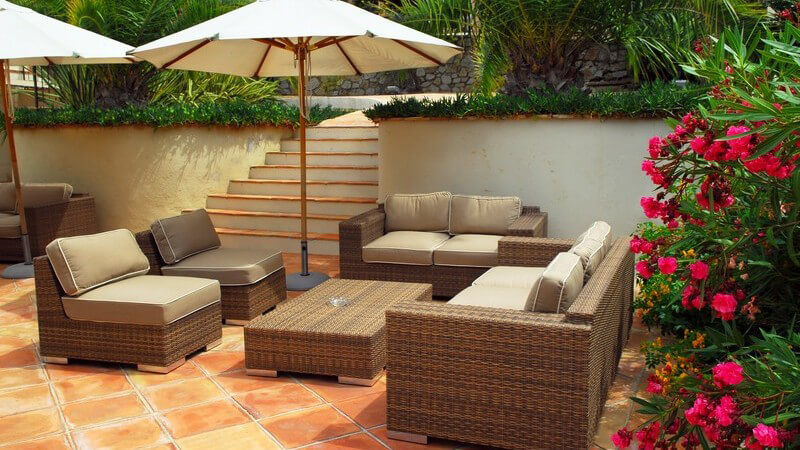 Terrasse mit weiß-braunen Gartenmöbeln und Sonnenschirm vor einer weißen Mauer mit Treppe