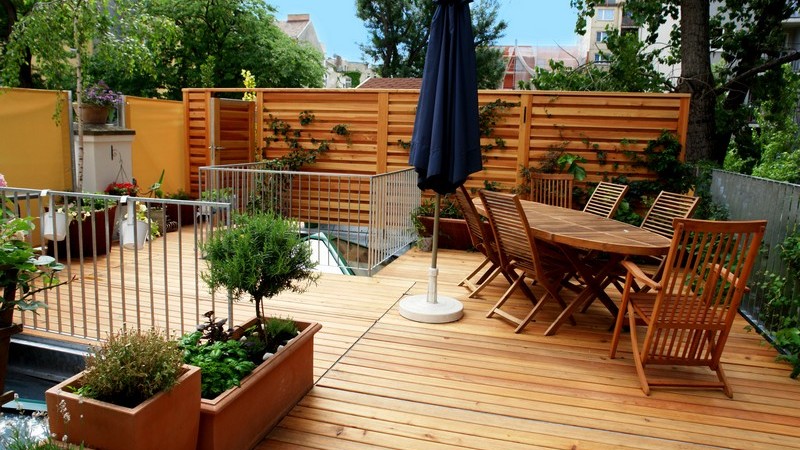 Großer Holzbalkon mit Gartenmöbeln, Pflanzen und Sonnenschirm