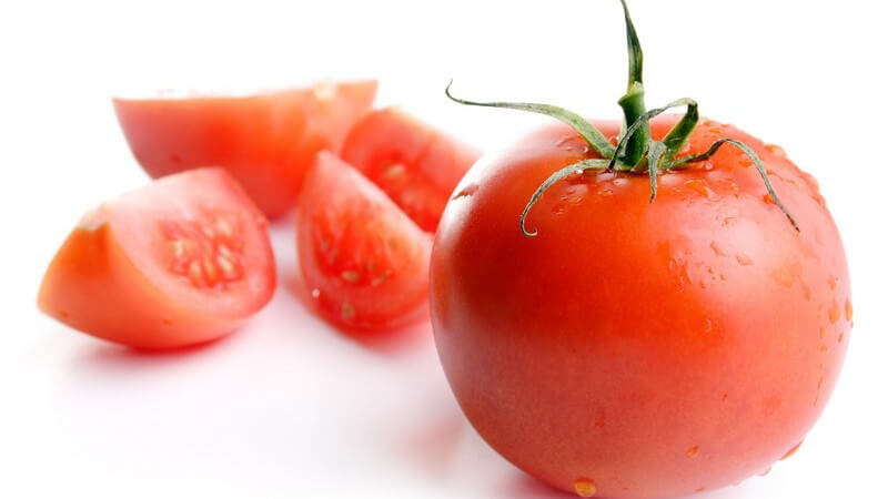 Frisch gewaschene Tomate, dahinter aufgeschnittene halbe Tomate