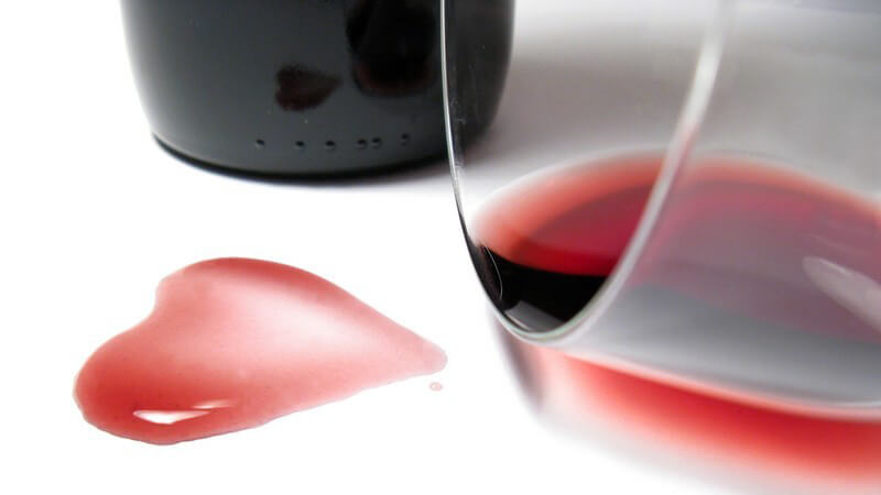 Umgekipptes Glas mit Rotwein, Rotweinfleck in Herzform, Rotweinflasche
