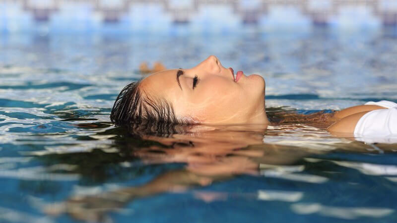Hübsche Frau in weißem Bikini beim Floating im Wasser, die Augen geschlossen