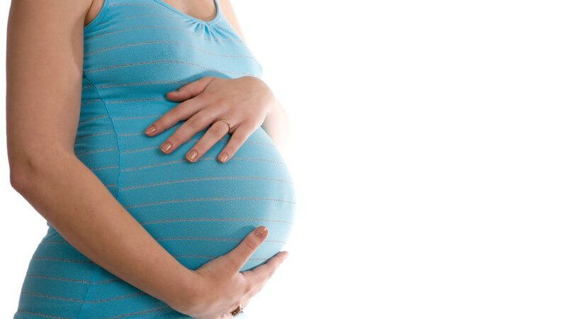 Schwangere Frau in blauem Top hält sich den Bauch mit beiden Händen