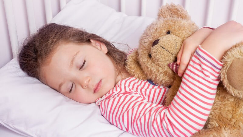 Kleines Mädchen schläft in ihrem Bett und hält einen Teddy im Arm