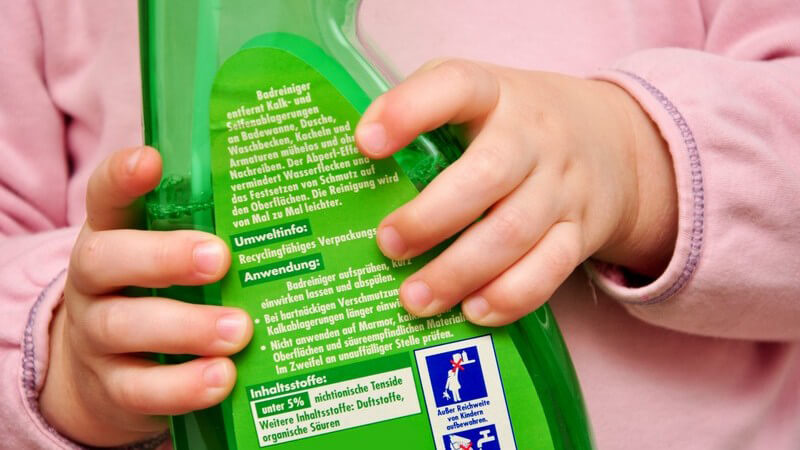 Hände eines Kleinkinds halten eine grüne Flasche mit giftigem Reinigungsmittel