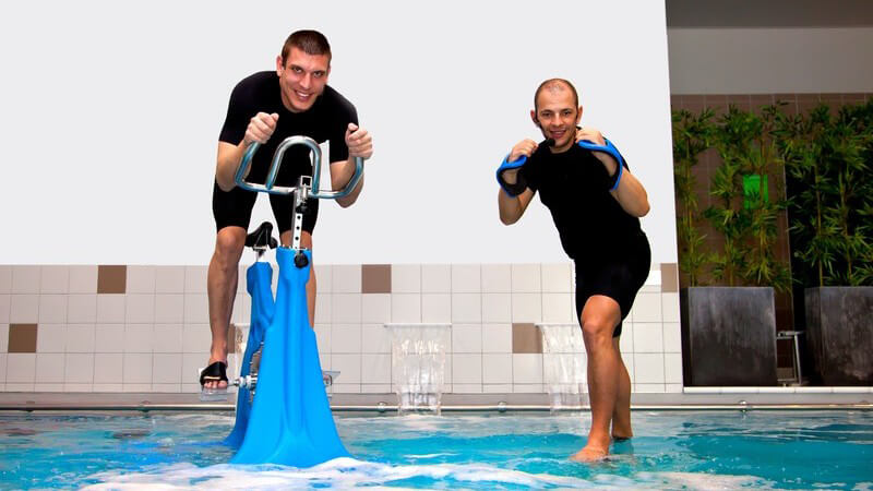 Zwei Männer machen Aqua-Fitness im Schwimmbad, einer sitzt auf einem Aqua-Bike