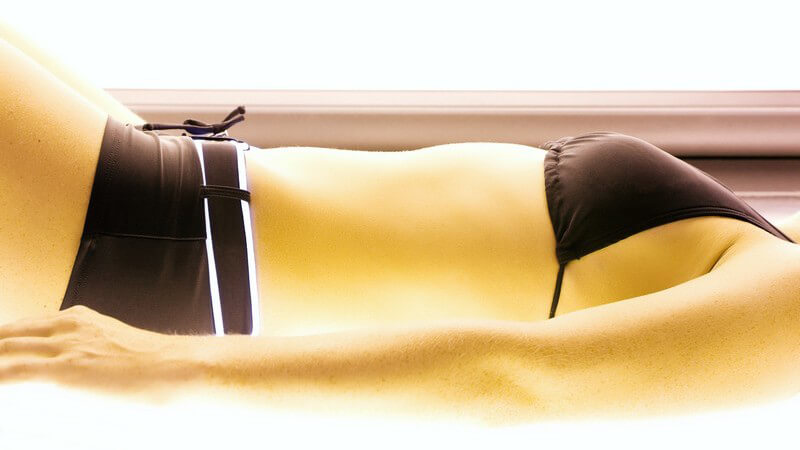 Körperausschnit Frau in schwarzem Bikini auf der Sonnenbank
