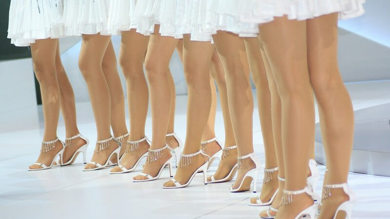Viele Frauenbeine in weißen High Heels und weißen Röcken, Models