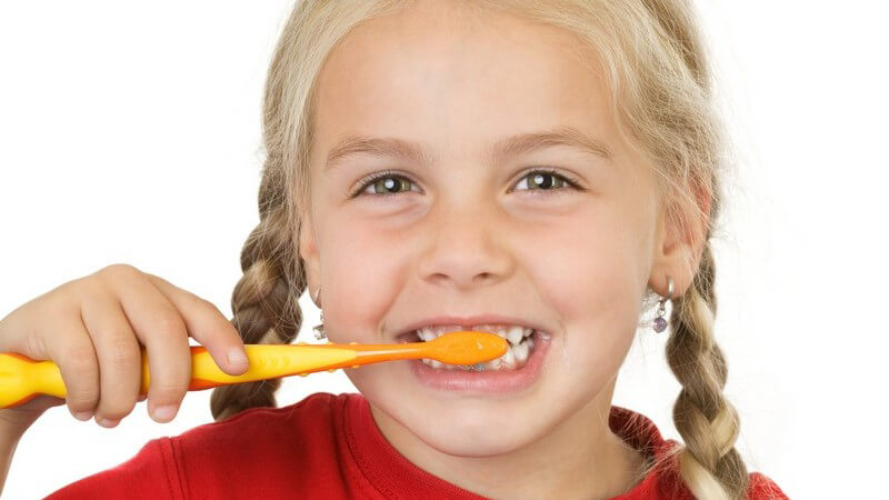Kleines Mädchen beim Zähneputzen lächelt in Kamera, weißer Hintergrund