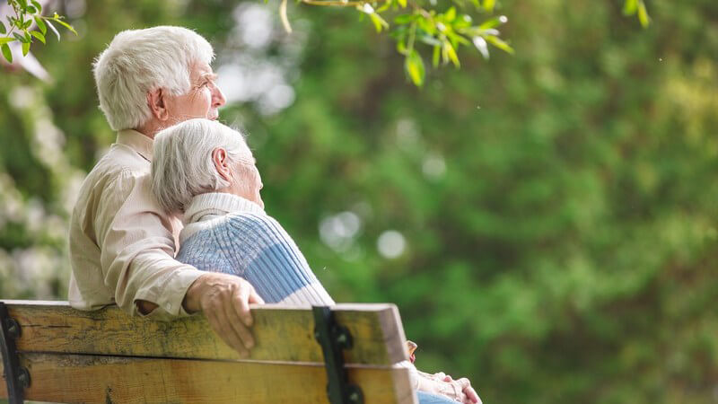 Seniorenpaar mit grauen Haaren sitzt auf einer Parkbank