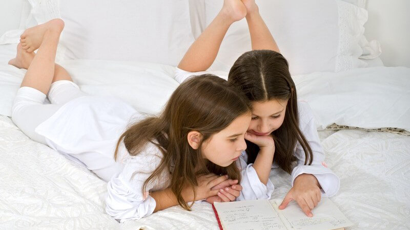 Zwei kleine Mädchen liegen im Bett und lesen ein Buch zusammen