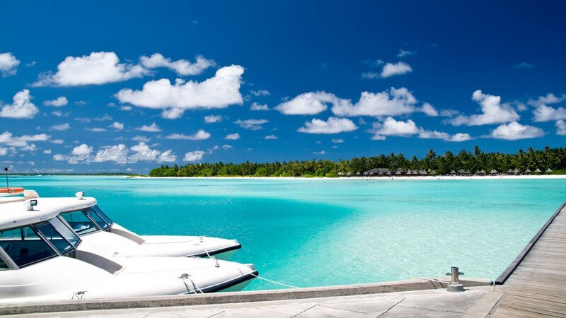 Zwei weiße Luxusyachten haben an Inselhafen angelegt, türkises Wasser, Strand und Palmen im Hintergrund, blauer Himmel