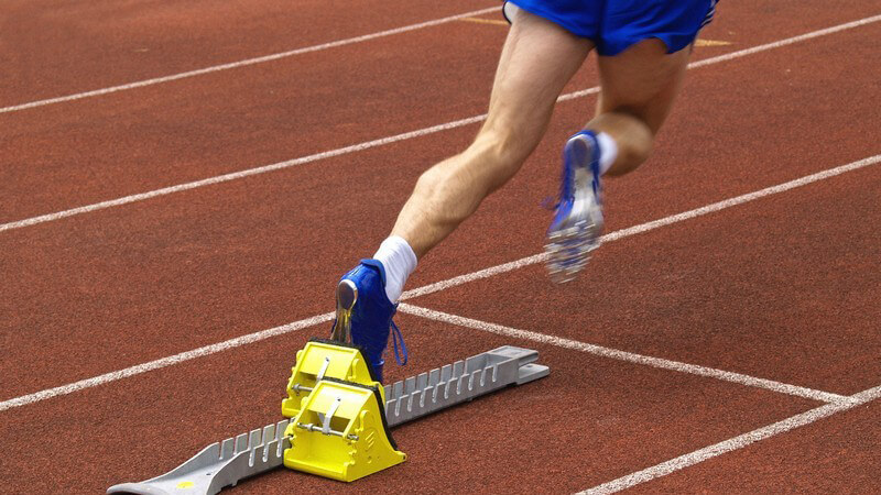 Beine eines Sprinters mit blauer Sporthose starten auf Sportplatz von Startblock
