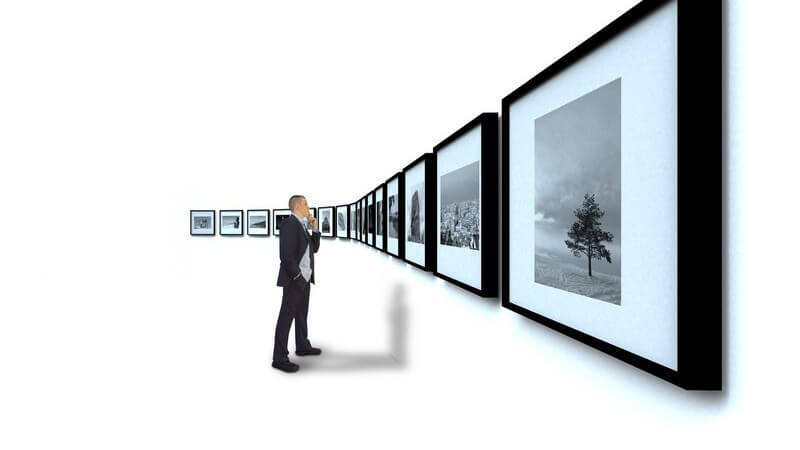 Mann im schwarzen Anzug begutachtet schwarz weiße Fotografien an weißer Wand