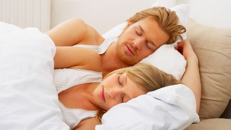 Blondes Paar liegt schlafend in weißem Bett