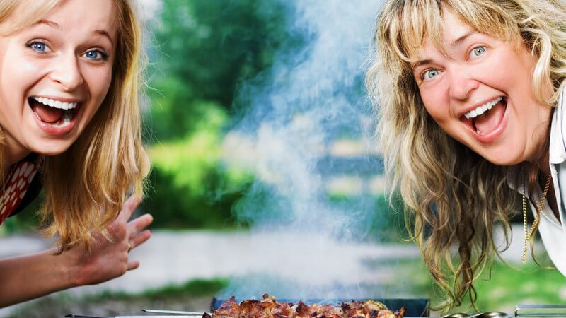 Zwei lachende Frauen über Grill mit Fleischspießen