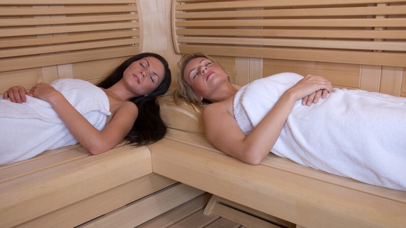 Zwei Freundinnen liegen in Handtüchern eingewickelt in der Sauna