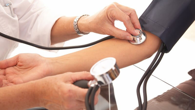 Zwei Hände einer Ärztin checkt oder überprüft den Blutdruck am rechten Arm einer Frau in Praxis