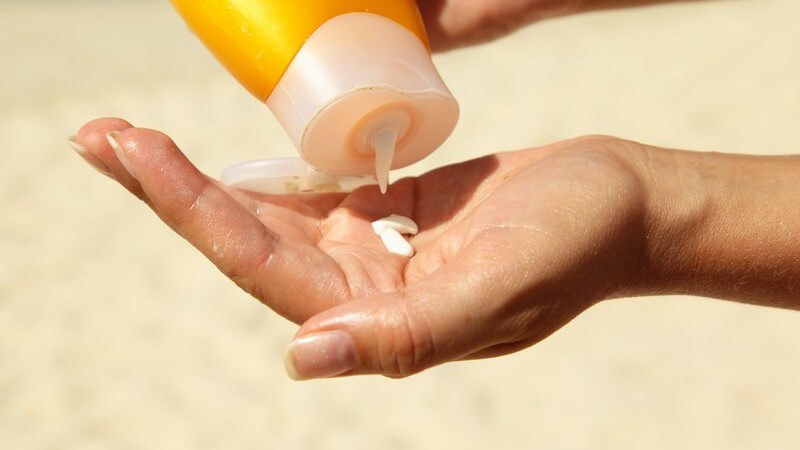 Frau am Strand drückt etwas Sonnencreme aus einer gelben Flasche in ihre Hand