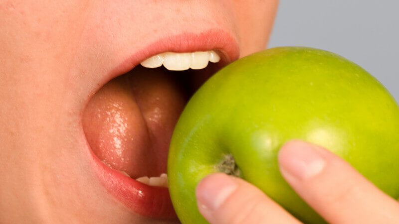 Geöffneter Mund, der in einen grünen Apfel beißt