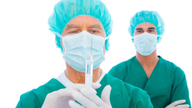 Zwei Chirurgen mit grünem Kittel und Mundschutz mit Spritze