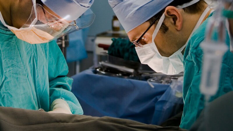 Operation - Zwei Chirurgen mit grünem Kittel und blauer Haube beim Operieren