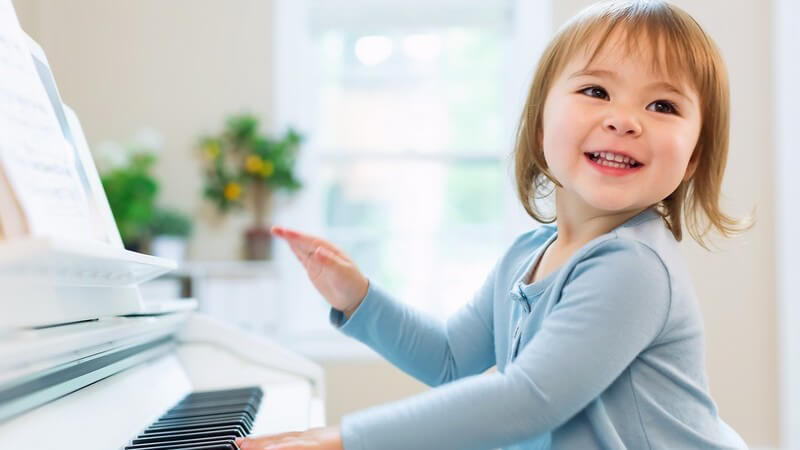 Kleines Mädchen in hellblauer Strickjacke spielt auf einem Klavier