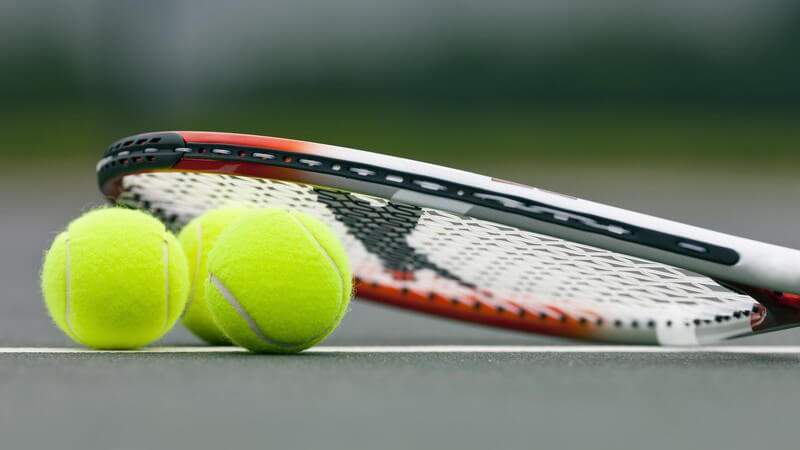 Tennisschläger auf drei Tennisbällen auf Tennisplatz