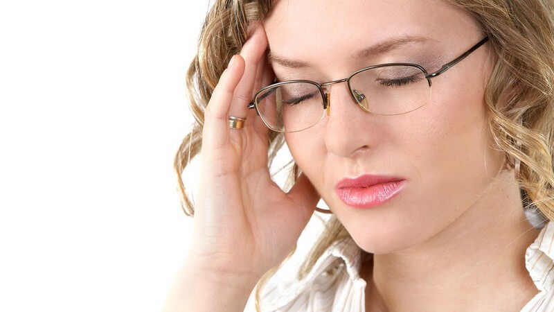 Kopfschmerzen - Blonde Frau mit Brille hat die Augen zu und fasst sich an die Schläfe