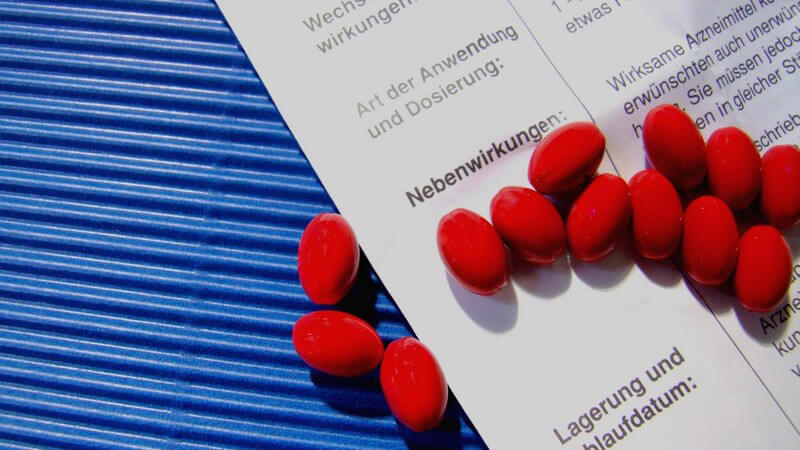 Rote Pillen auf einem Beipackzettel mit der Aufschrift Nebenwirkungen