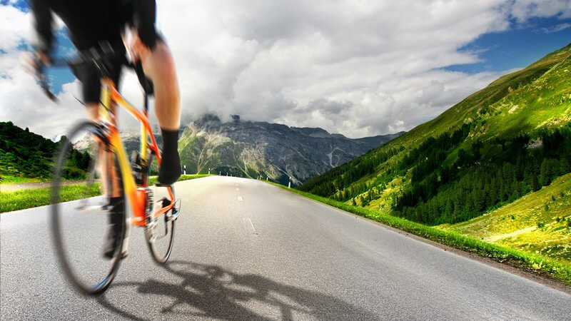 Mann auf Rennrad auf Straße, im Hintergrund Berge