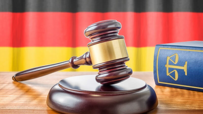 Richterhammer neben blauem Gesetzbuch vor Deutschlandflagge