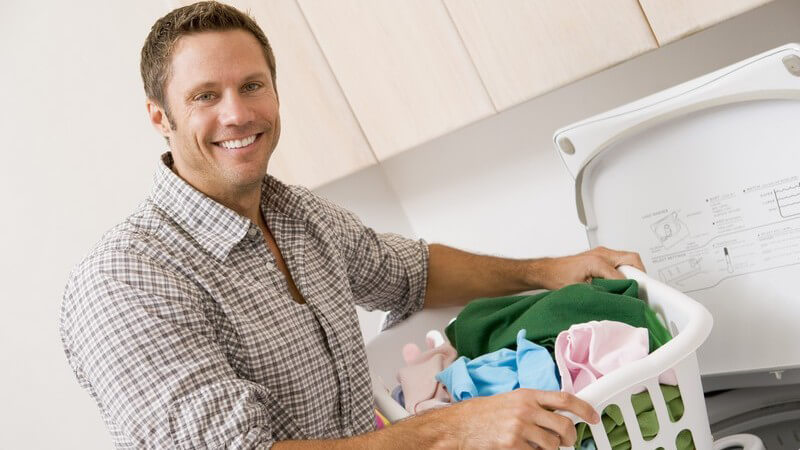Lächelnder Mann an mit Wäschekorb steht an Waschmaschine