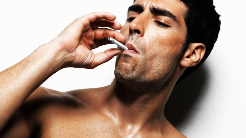 Mann mit nacktem Oberkörper an Wand gelehnt raucht, Macho
