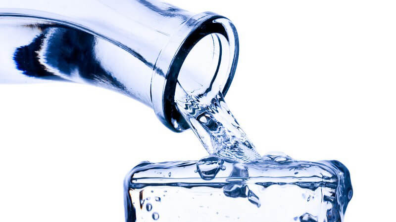 Eine Glasflasche füllt ein Glas Wasser bis zum Anschlag