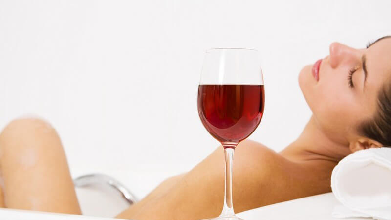 Junge Frau liegt entspannt in der Badewanne, neben ihr ein Glas mit Rotwein