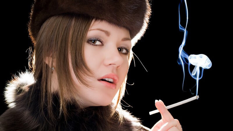 Junge Frau in Pelz und Pelzmütze beim Rauchen, schwarzer Hintergrund
