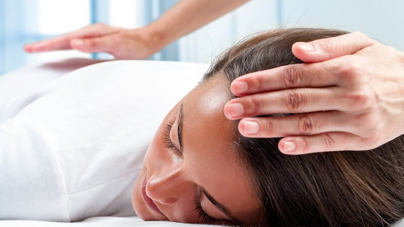 Frau liegt bei einer Reiki-Behandlung auf dem Bauch, Hände des Therapeuten liegen auf Rücken und Kopf
