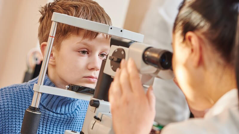 Junge in blauem Rollkragenpullover wird von Augenärztin untersucht
