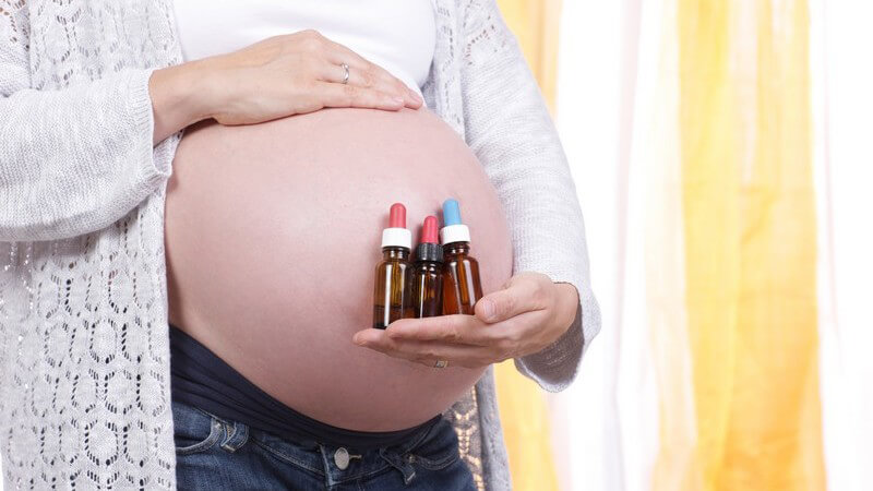 Schwangere Frau hält drei Arzneifläschchen mit Bachblüten vor den dicken Babybauch