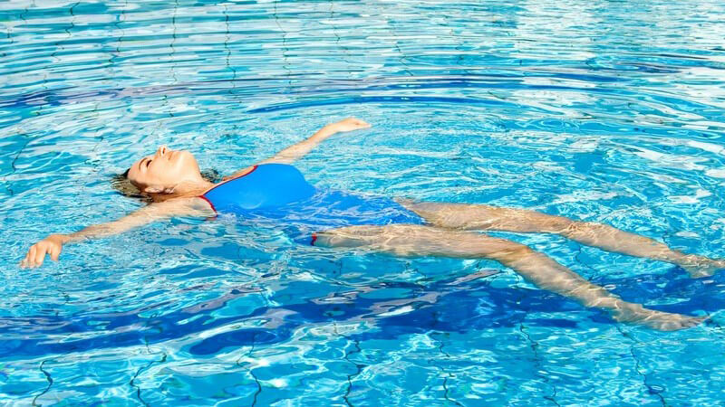 Junge Frau in blauem Badeanzug im Schwimmbad lässt sich auf Rücken im Wasser treiben