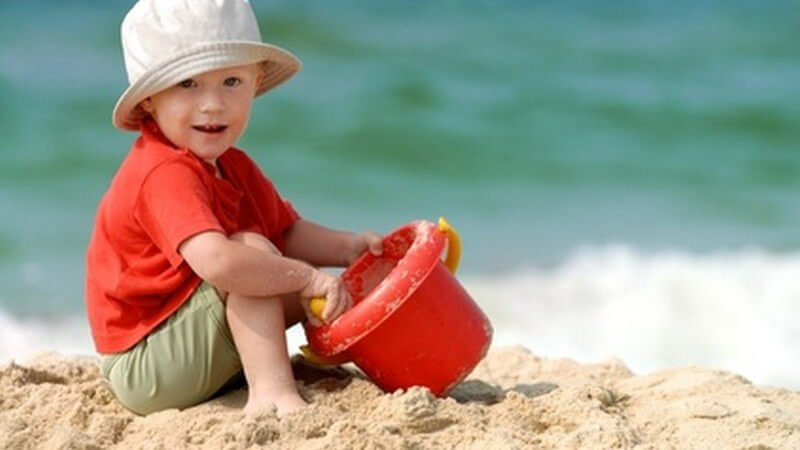 Kleiner Junge mit Hut spielt mit Eimer und Schaufel am Strand