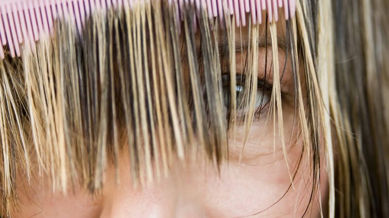 Dunkelhaarige Frau mit blonden Strähnen kämmt Haare vor Gesicht
