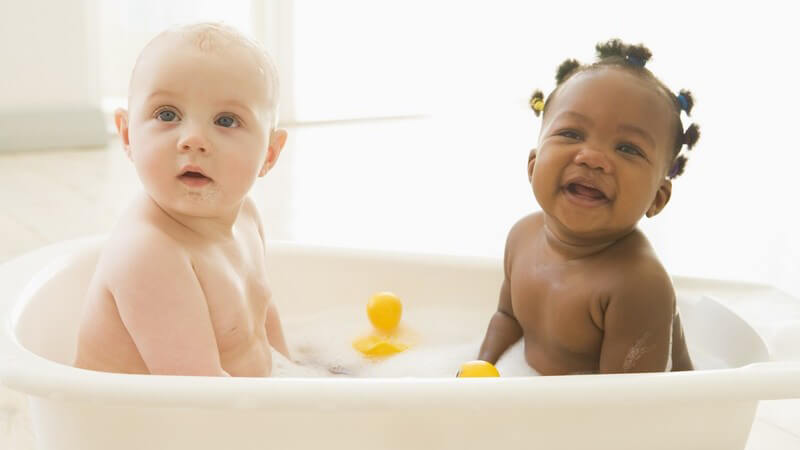 Weißes und farbiges Baby in Badewanne mit Badeenten und Schaum